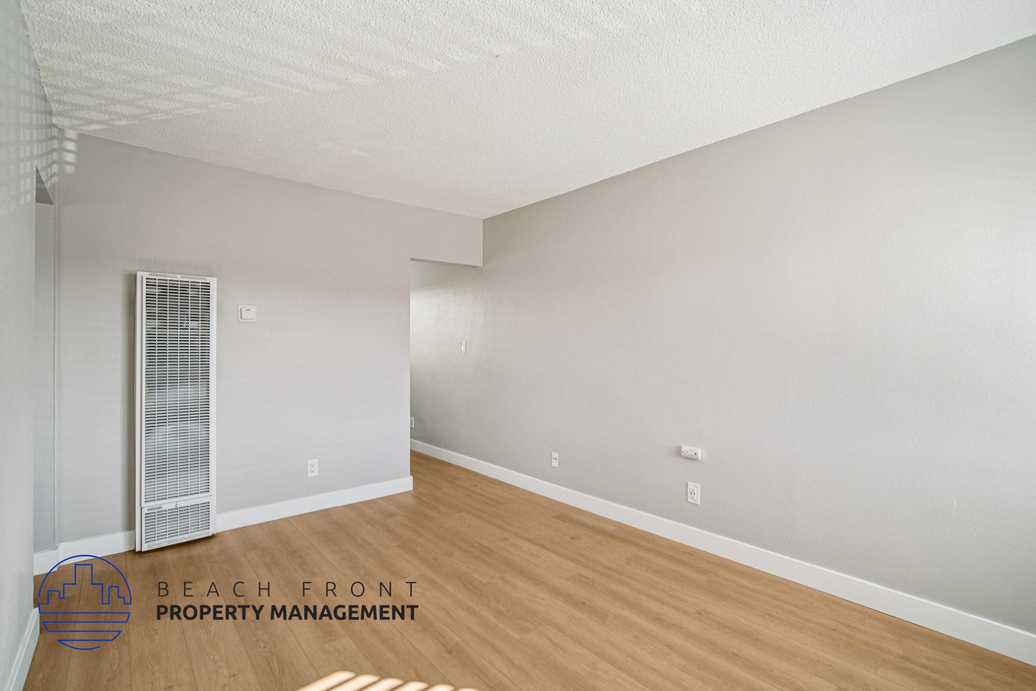 A spacious room with a wooden floor and a window with blinds.